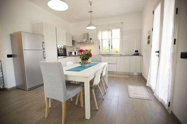 Une cuisine moderne avec des meubles blancs, un réfrigérateur en acier inoxydable et une table à manger avec des chaises.