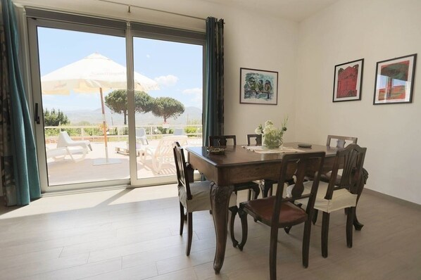 A dining area with a table and chairs, a view of the outdoors, and artwork on the wall.