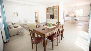 A spacious living area with a dining table, chairs, and a sofa. A kitchen is visible in the background. - Villa NELLA, relax and amazing view (Sicilia)
