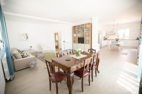 A spacious living area with a dining table, chairs, and a sofa. A kitchen is visible in the background.
