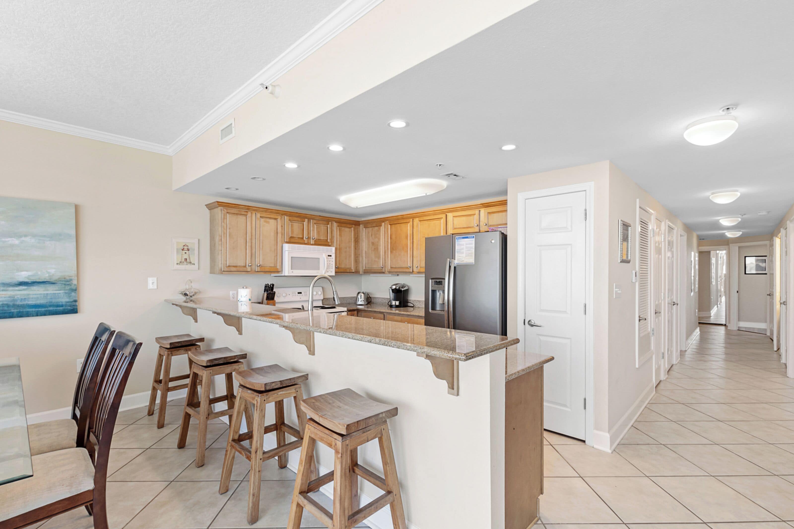 A spacious kitchen with wooden cabinets, a central island with stools, a refrigerator, and a microwave.