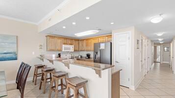 A spacious kitchen with wooden cabinets, a central island with stools, a refrigerator, and a microwave.
