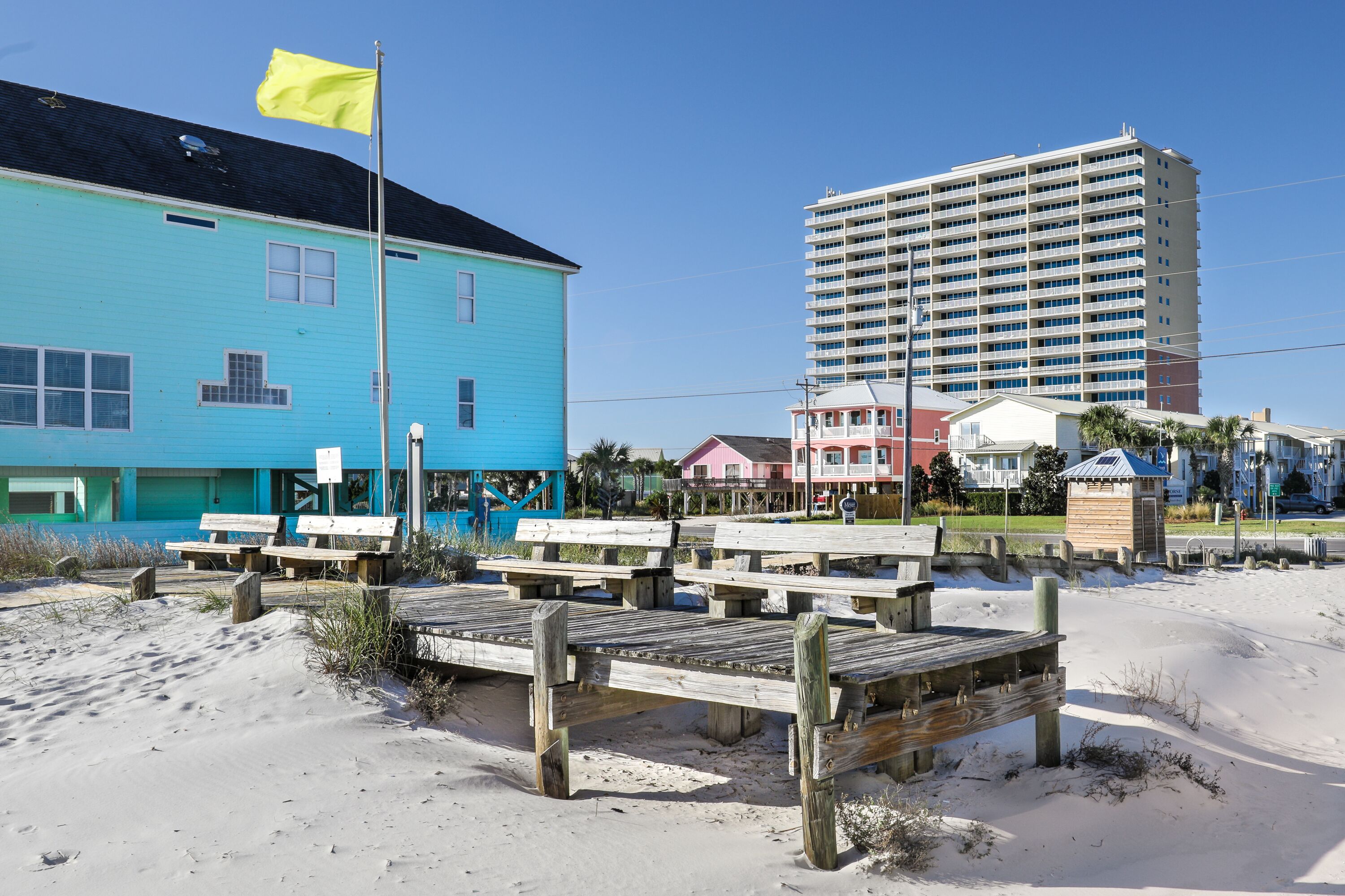 A beachside hotel with a blue building, wooden deck, and a tall hotel structure in the background.