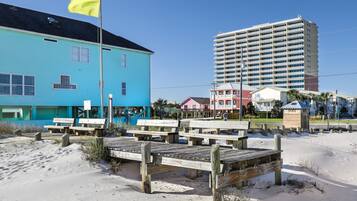 A beachside hotel with a blue building, wooden deck, and a tall hotel structure in the background.