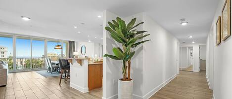 A modern interior with a large potted plant, a dining area, and a view through large windows.