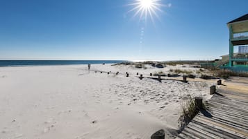 Een strand met een houten loopplaquette die naar een gebouw met een balkon leidt.