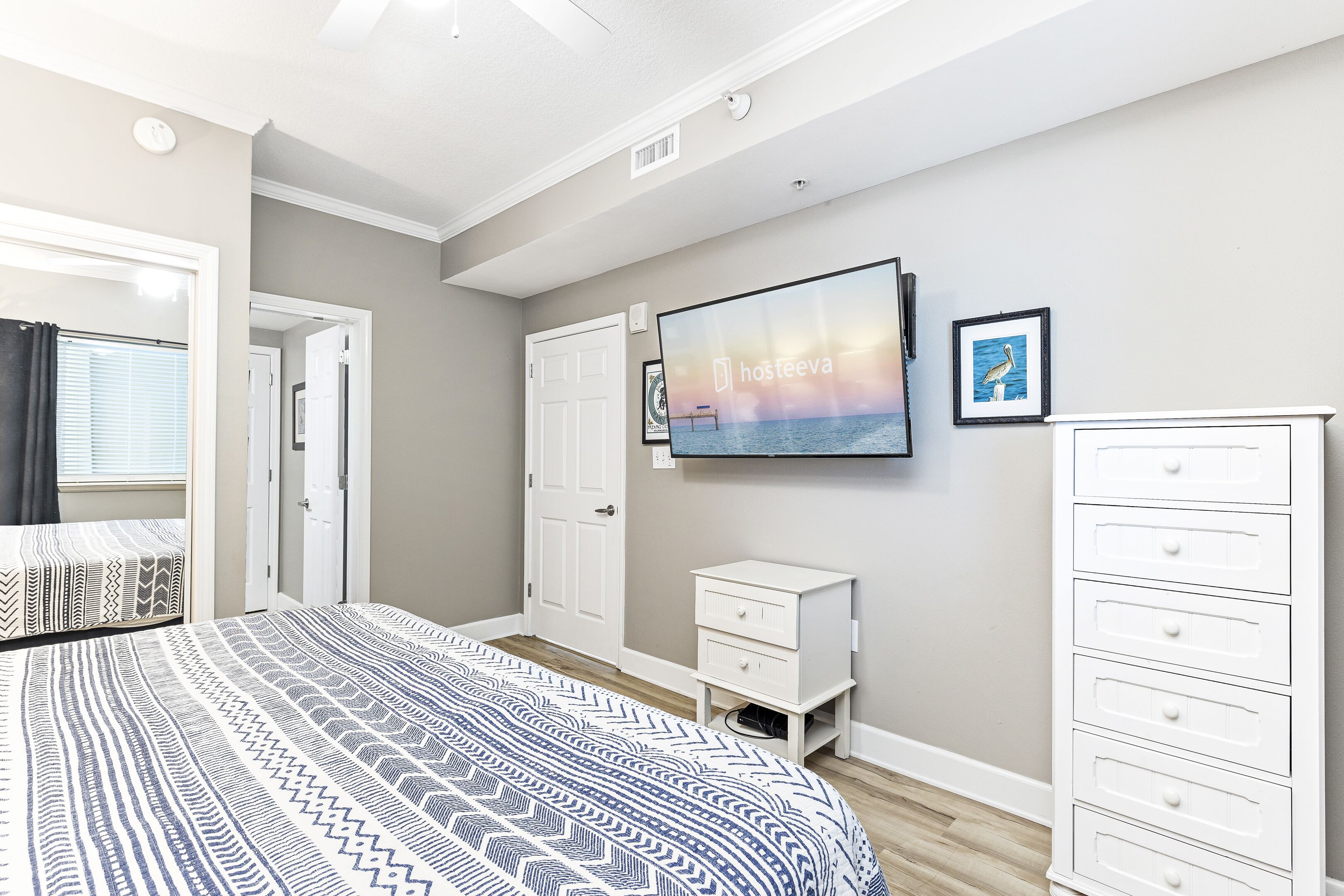 Une chambre à coucher avec un lit, une commode, une table de chevet, un téléviseur et un tableau encadré accroché au mur.