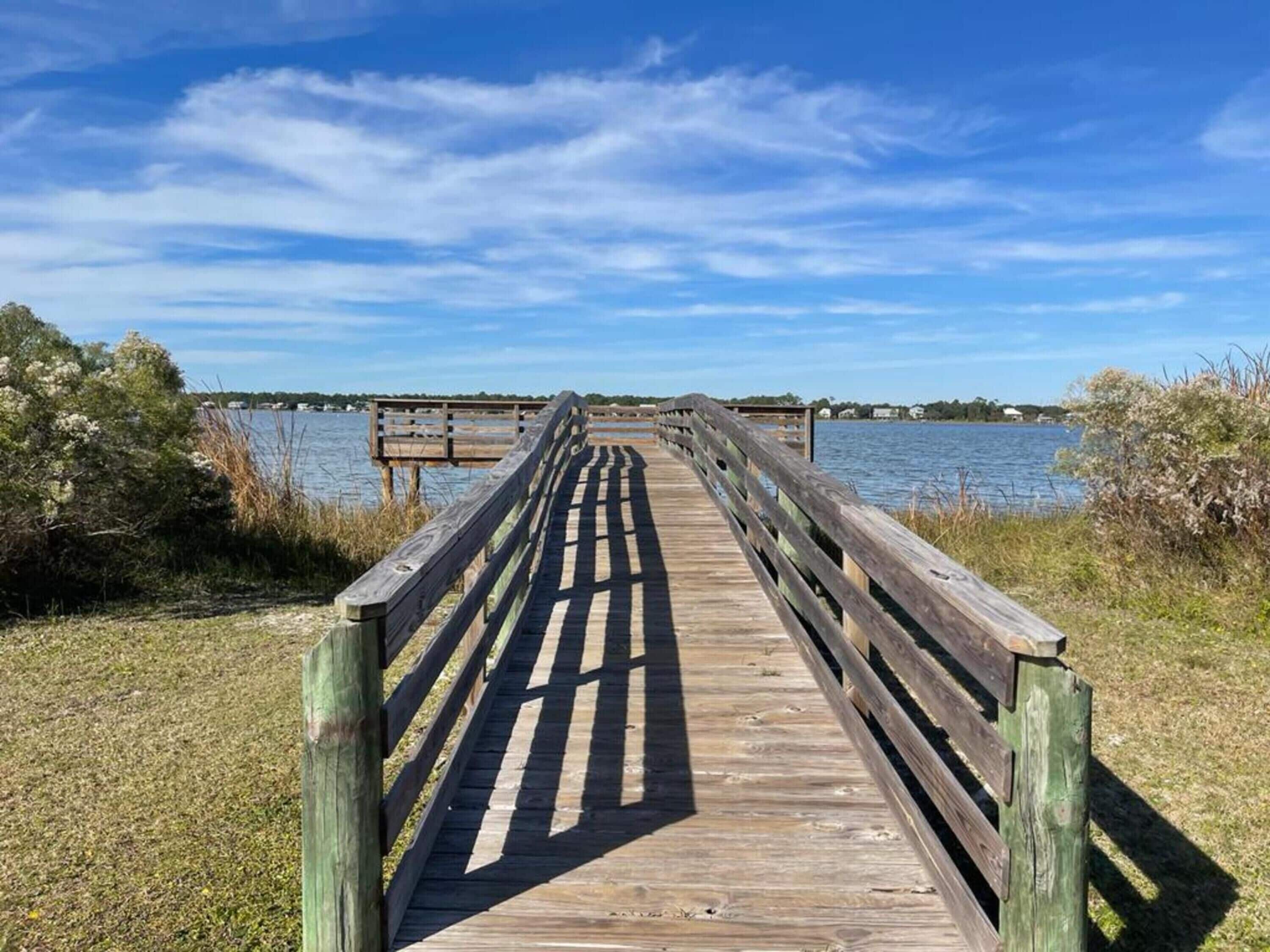 A wooden boardwalk leading to a dock over water, surrounded by grassy areas and trees.