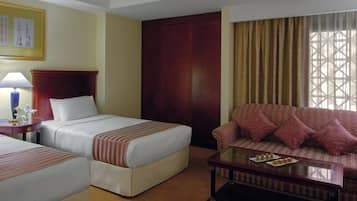 A hotel room with a bed, a sofa, a table with a tray of food, a lamp, and a window with curtains.