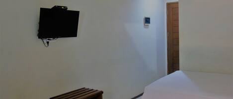 A hotel room with a bed, a small wooden nightstand, a television mounted on the wall, and a door leading to another room.