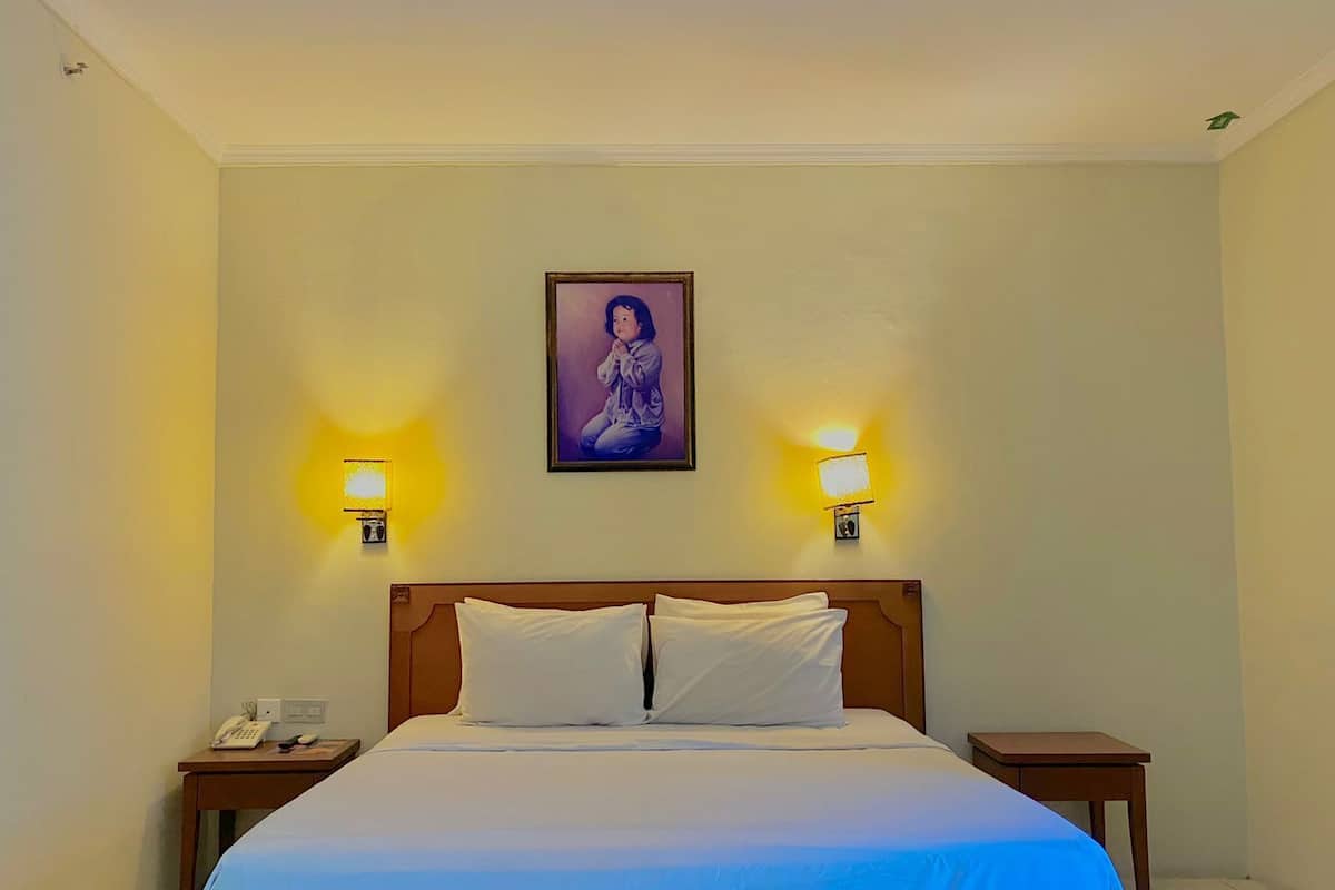 Ein Hotelzimmer mit einem großen Bett, zwei Nachttischen, einer Wandlampe und einem gerahmten Bild über dem Bett.