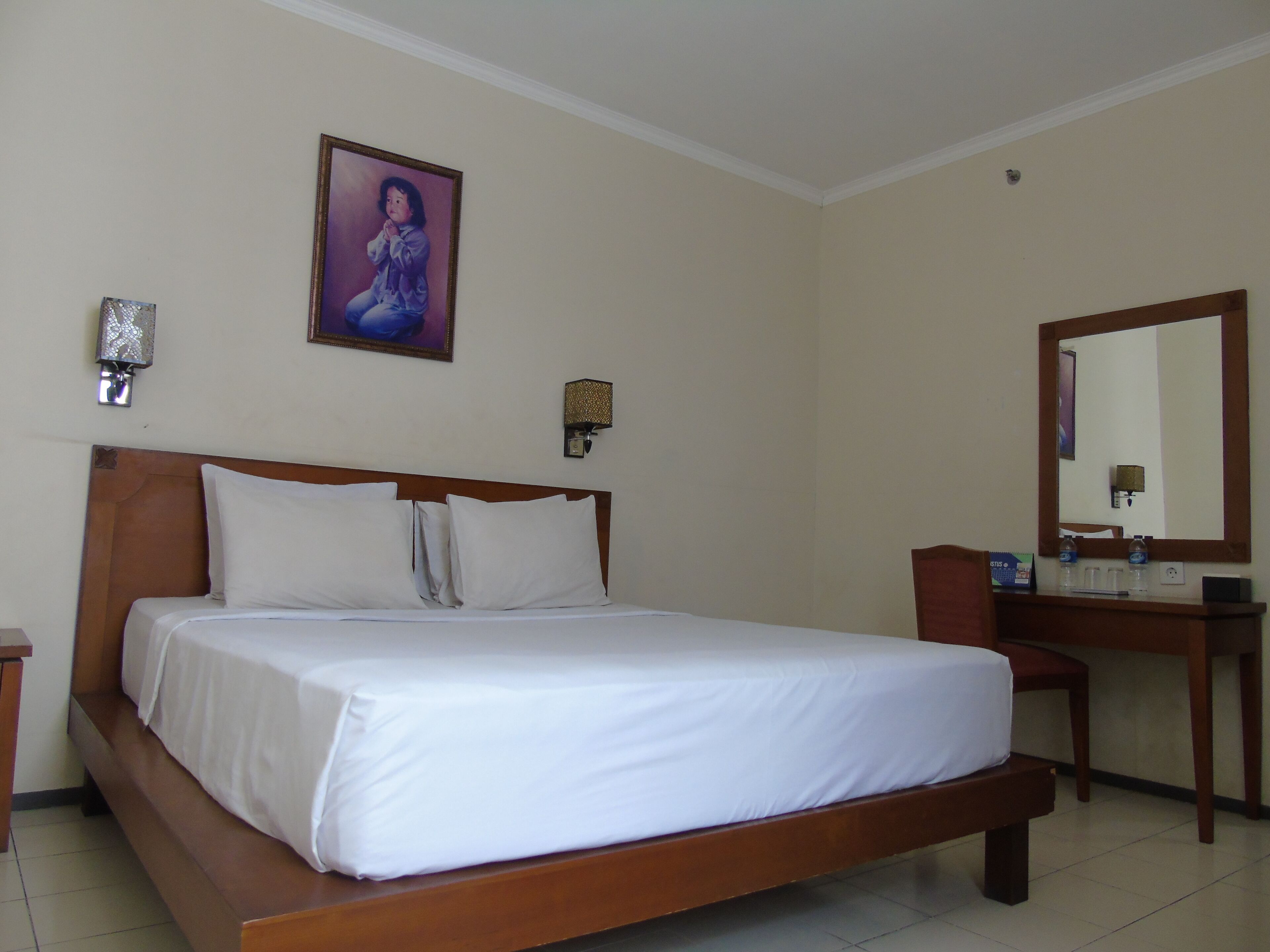 A hotel room with a wooden bed, white bedding, a large mirror, and a framed picture on the wall.