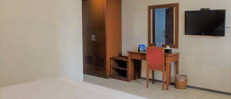 A hotel room with a bed, a desk, a chair, a wardrobe, a television, and a trash bin.