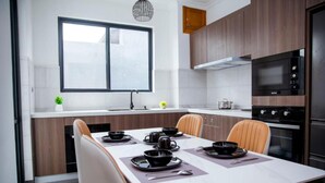 A modern kitchen with a dining table set for four, equipped with a microwave, oven, and a window above the sink. - Rose Aparthotel (Kigali)