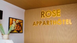 A reception desk with a marble top and a wooden panel wall behind it. The wall has the text "ROSE APPARTHOTEL" in gold letters. - Rose Aparthotel (Kigali)