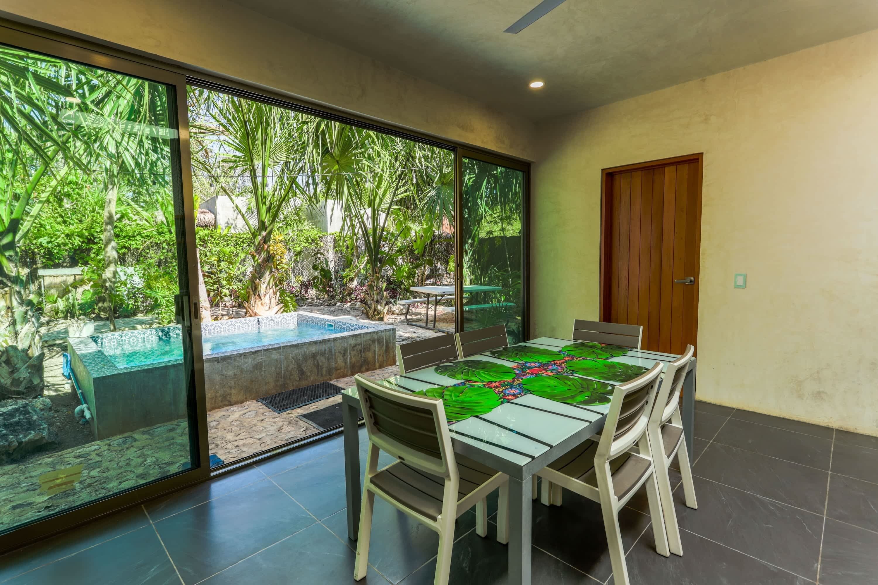 Zona pranzo con tavolo e sedie in vetro, una porta e vista su un giardino con vasca idromassaggio.