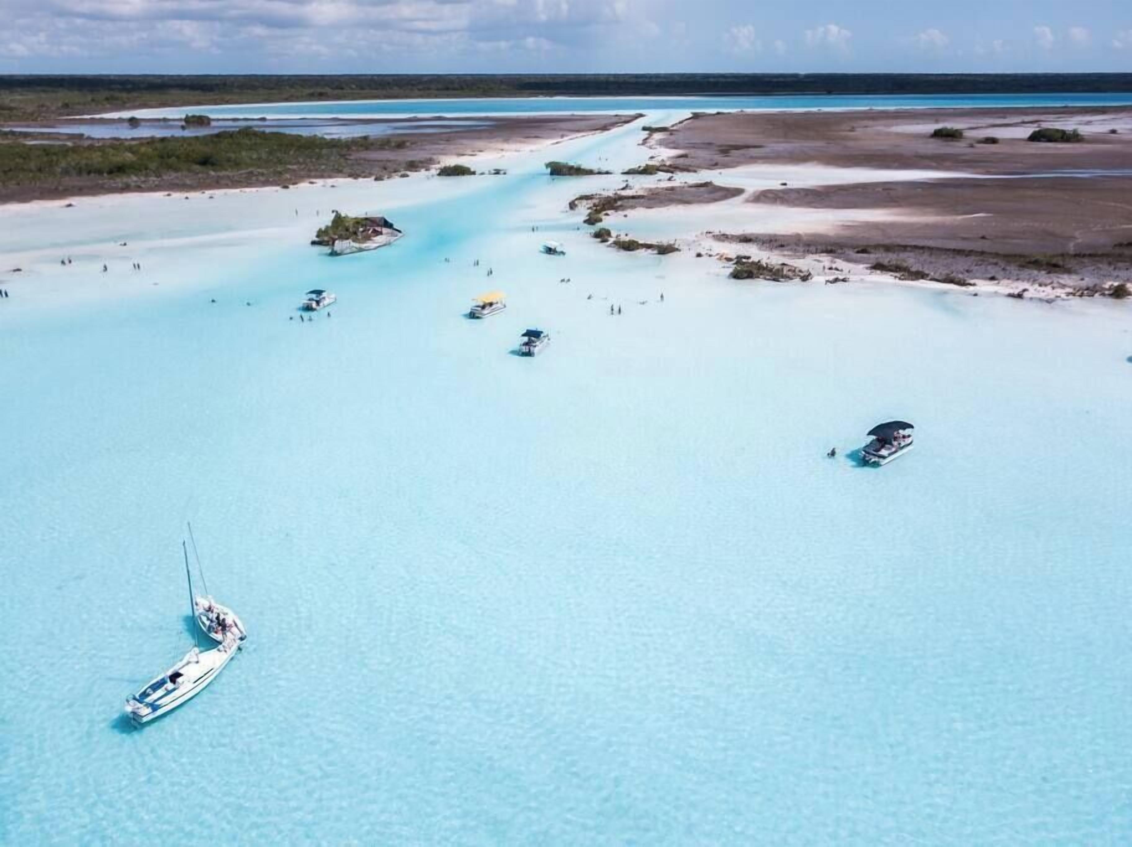 An aerial view of a coastal area with clear turquoise waters, boats, and a small island with a structure.