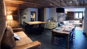 Un salon moderne avec un plafond en bois, un coin repas avec une table dressée pour quatre personnes et un canapé.