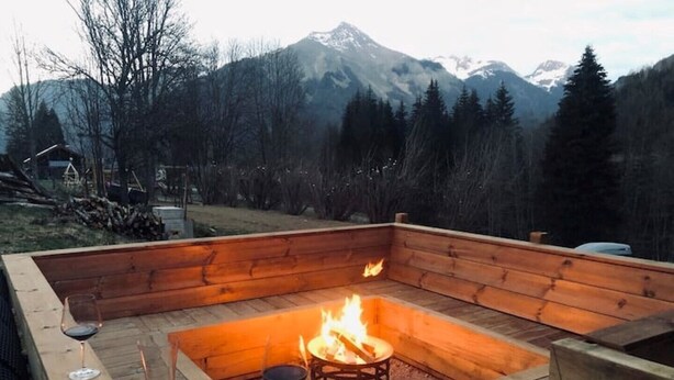 Un foyer en bois, entouré de sièges, avec une vue sur les montagnes en arrière-plan.