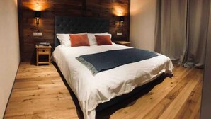 Une chambre avec un grand lit, un plancher en bois et deux lampes fixées au mur.
