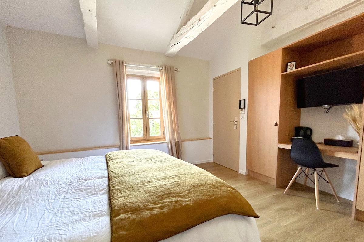 A bedroom with a bed, a desk, a chair, a television, and a window with curtains.