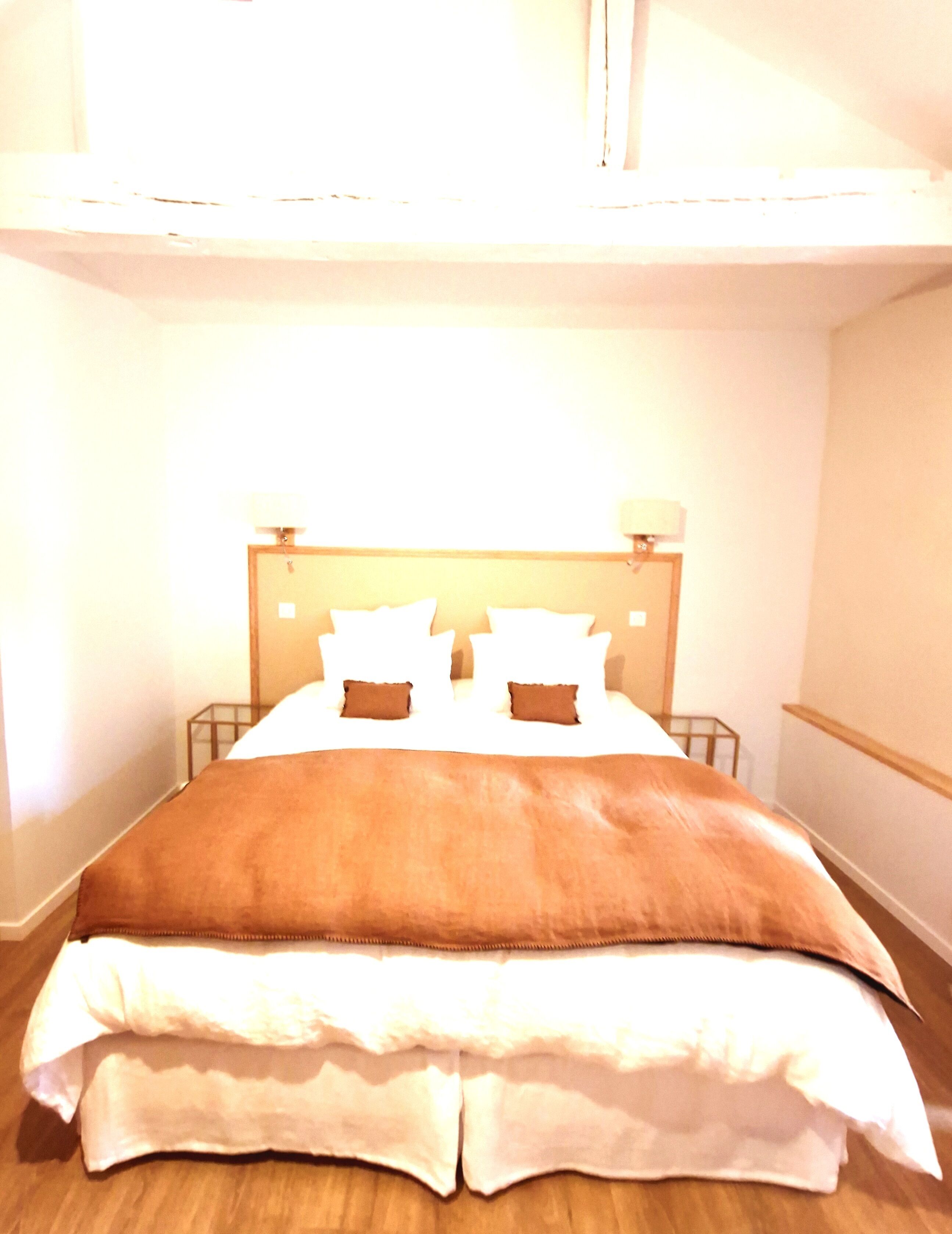 Una cama con cabecera de madera, ropa de cama blanca y dos lámparas de noche.