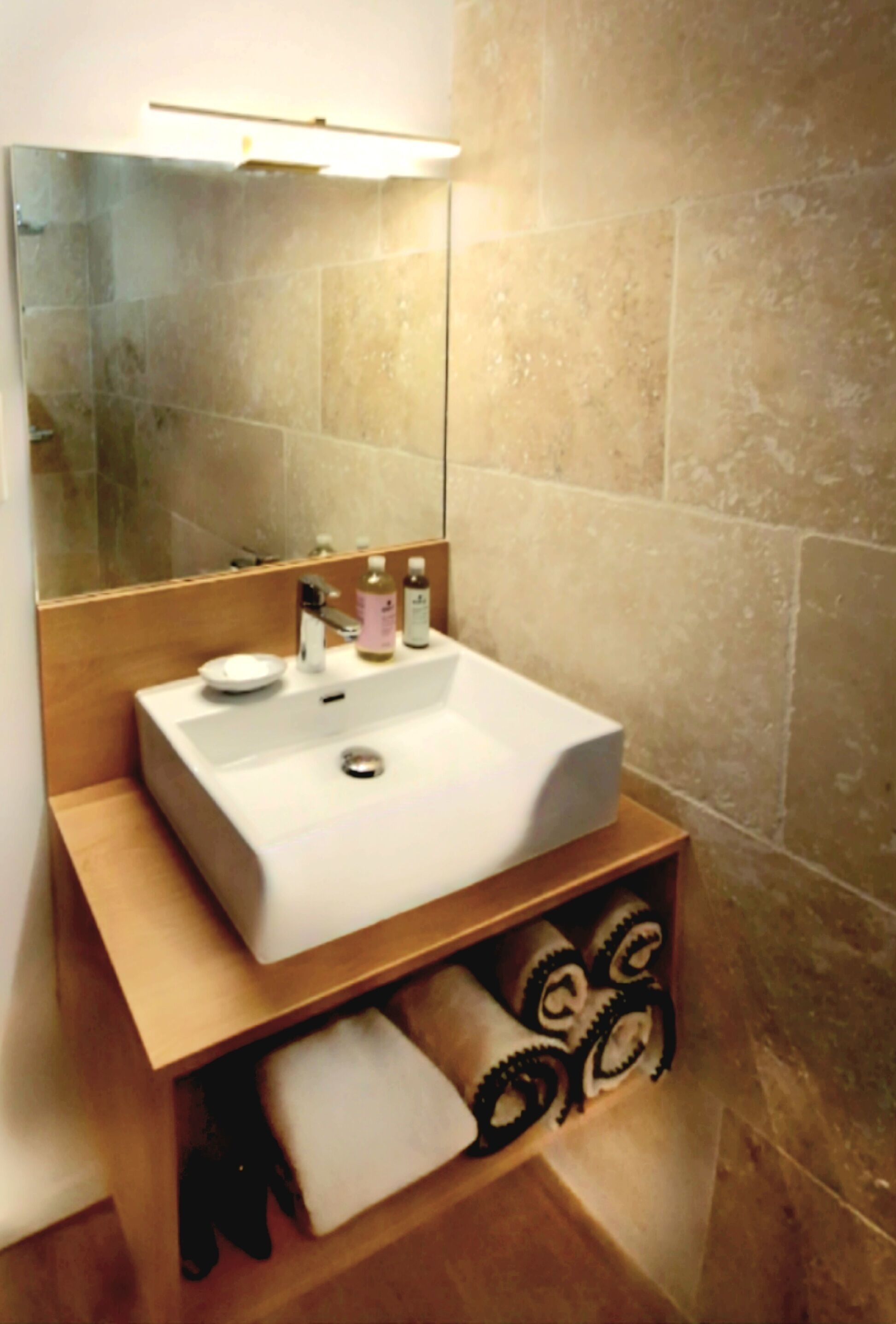 Une salle de bain avec un lavabo blanc, un miroir et des murs recouverts de carreaux beiges.