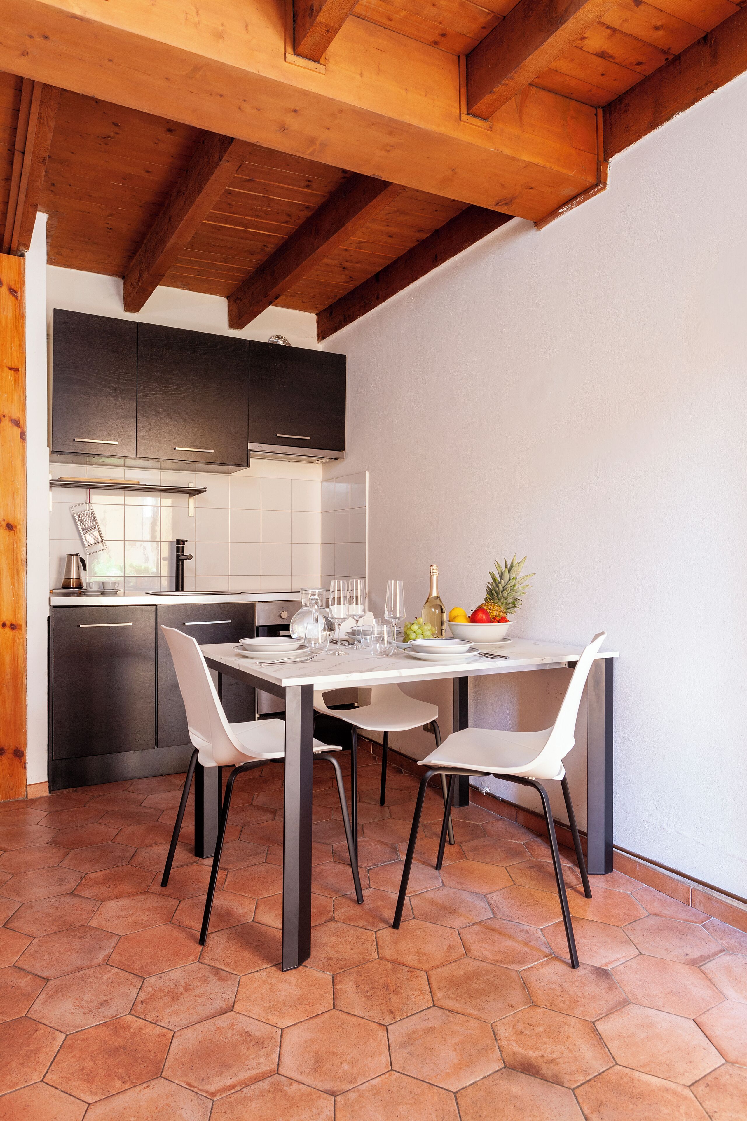 Una cocina moderna con armarios oscuros, encimera blanca y una mesa de comedor preparada para cuatro comensales.
