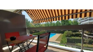 A balcony with a striped awning, a red chair, and a table. - Allées du Parc, high-end apartment 🌳🌲🌾 (Dijon)