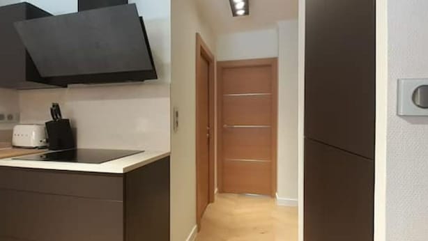 A compact kitchen with a built-in stove, a microwave, and a coffee maker. A wooden door leads to a hallway. - Allées du Parc, high-end apartment 🌳🌲🌾 (Dijon)