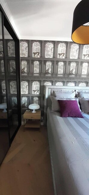 Une chambre à coucher comprenant un lit, une table de chevet, une lampe et un mur orné d’un motif décoratif.