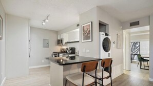 A modern kitchen with a central island, microwave, oven, and a washing machine. - Chelsea #249 xxxxxxx (Austin)