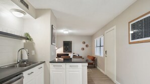 A modern kitchen with white cabinets, a black countertop, and a built-in oven. There is a window with blinds, a plant, and a framed artwork on the wall. - Chelsea #249 xxxxxxx (Austin)