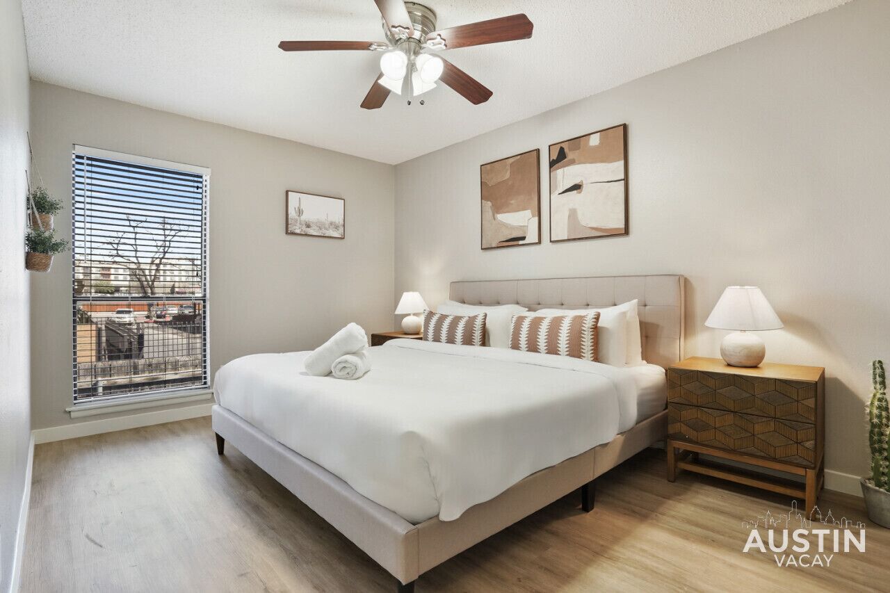 Un dormitorio con una cama, un ventilador de techo, una mesita de noche y una ventana con persianas.