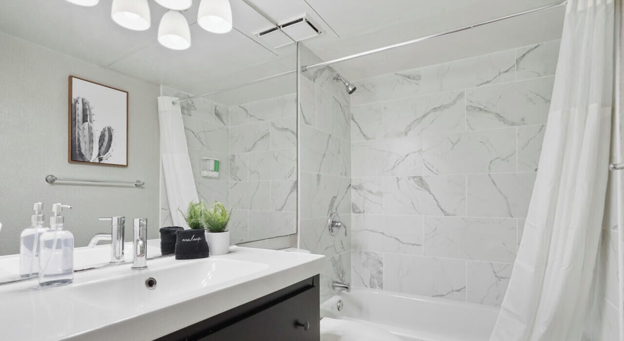 A modern bathroom with a marble shower, a white sink with toiletries, and a toilet.