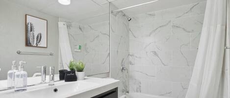 A modern bathroom with a marble shower, a white sink with toiletries, and a toilet.
