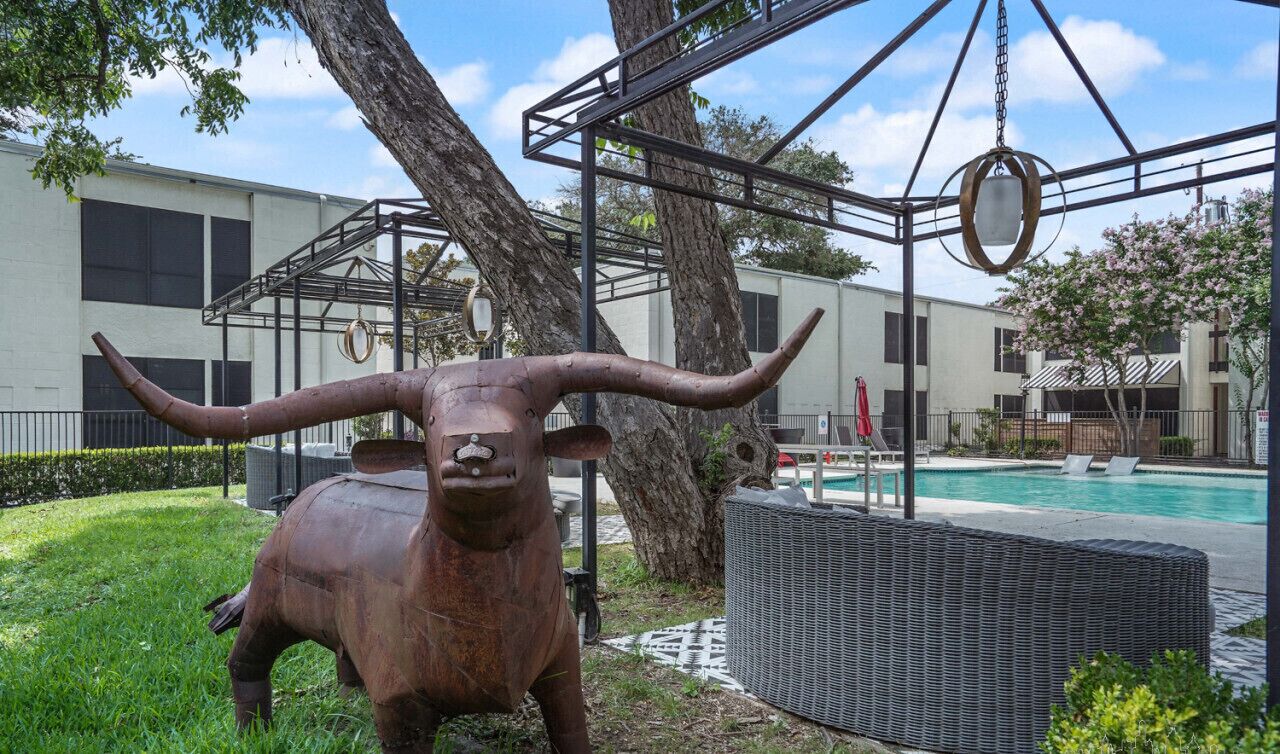 A bull statue in a grassy area with a pool and a building in the background.