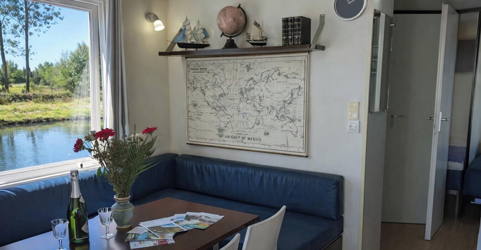 Um quarto com um mapa grande na parede, uma janela com vista para a água, um sofá azul e uma mesa com uma garrafa e copos.