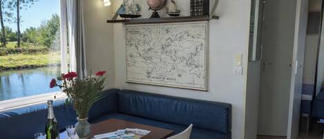 A room with a large map on the wall, a window with a view of a body of water, a blue sofa, and a table with a bottle and glasses.