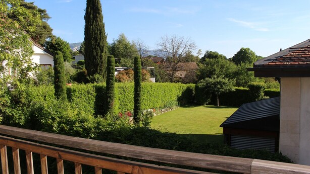 Un jardin résidentiel agrémenté d’une terrasse en bois, d’une pelouse et de divers arbres et arbustes.