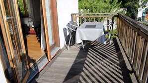 Une terrasse en bois avec une table et des chaises, une porte vitrée et une vue sur la verdure.