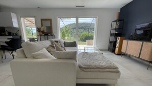 A modern living room with a sofa, ottoman, and a glass coffee table. There is a dining area with chairs and a table, and a TV on a stand. - Pretty villa in the Bandol vineyards, 15 minutes from the beaches. (Le Beausset)