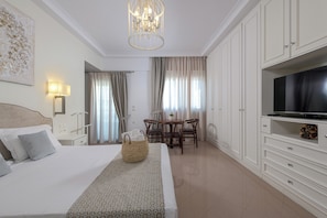 A hotel room with a bed, a TV, a dining area, and a chandelier.