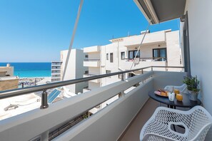 Un balcón con vista al mar, una mesa con alimentos para el desayuno y una silla blanca.