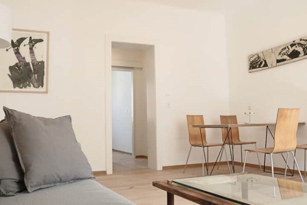 A modern living room with a sofa, a glass coffee table, and a dining area with chairs and a table.