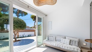 Ein modernes Wohnzimmer mit einer Couch, einem runden Teppich und einer Glastür, die auf eine Terrasse mit Pool und Garten führt.
