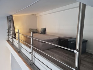 A compact, modern room with a bunk bed, a small bedside table, and a trash bin.