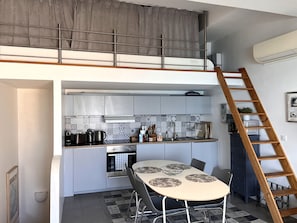 A compact kitchen with a dining area, a loft bedroom with a bunk bed, and a wooden ladder to the loft.