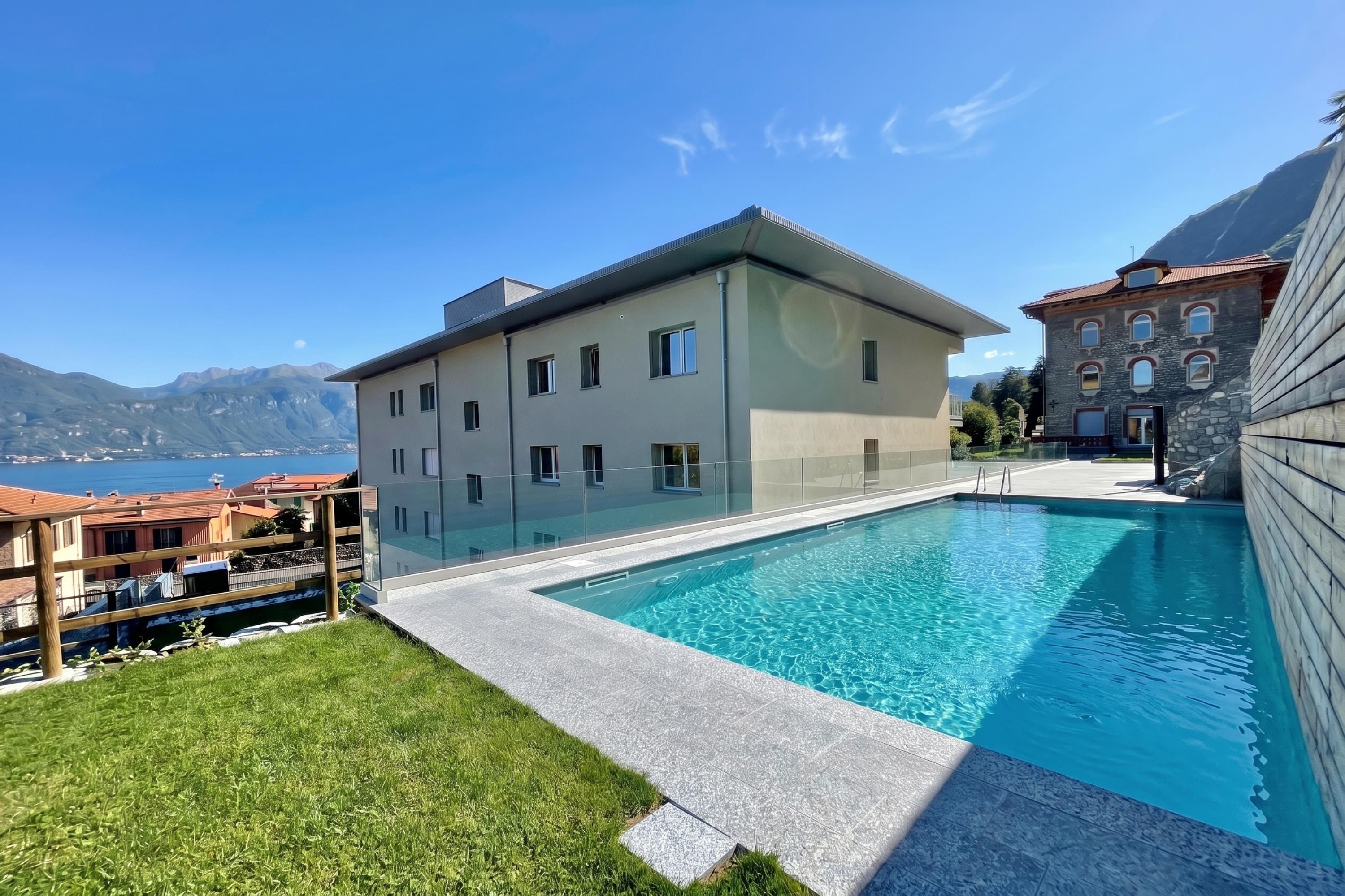 A modern building with a swimming pool, surrounded by a well-maintained lawn and a view of mountains.