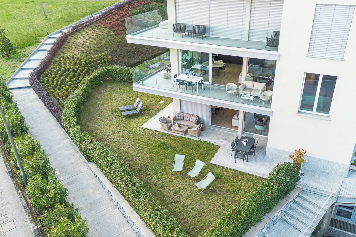A modern two-story building with a glass balcony, outdoor seating area, and a well-maintained lawn.